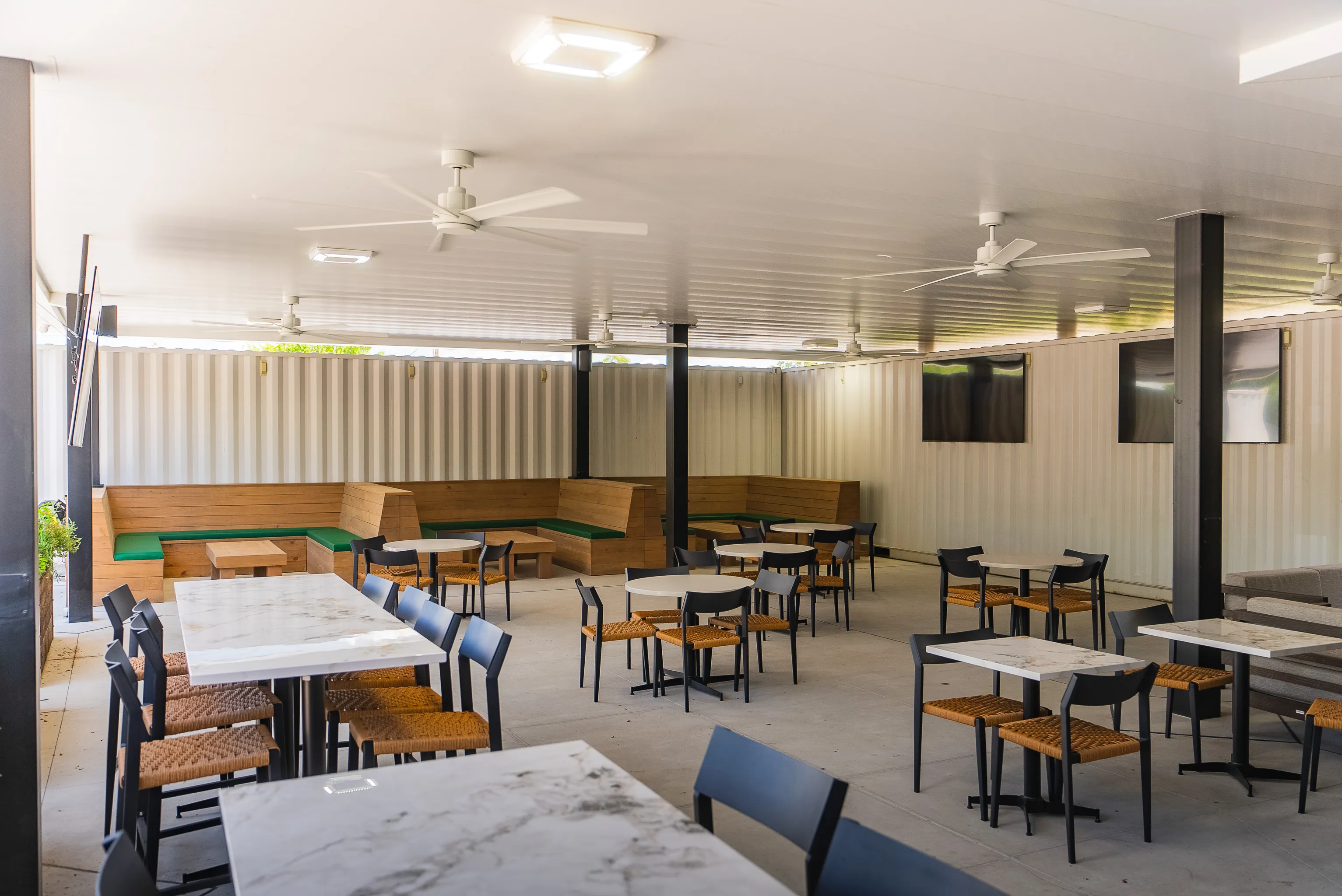 Modern outdoor patio dining area with tables, chairs, and ceiling fans.